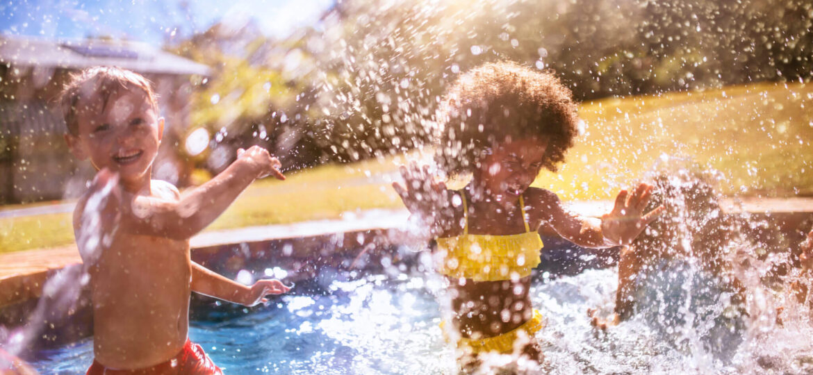 Little Afro girl and friend splashing water in swimming pool