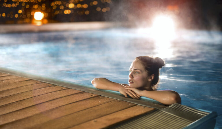 Young woman relaxing in heated swimming pool during winter night
