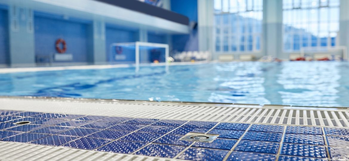 Focus on wet floor of blue poolside with white plastic grid against pool