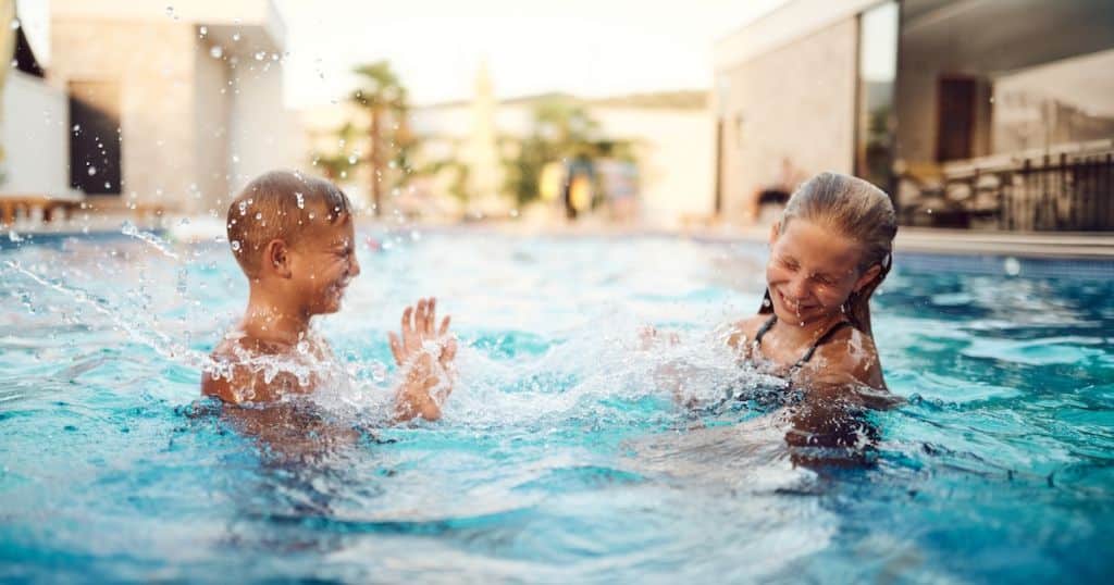 Two children laughing and splashing in a clean, clear outdoor AOP pool enjoying swimming without chlorine irritation or skin sensitivity