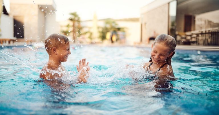 Two children laughing and splashing in a clean, clear outdoor AOP pool enjoying swimming without chlorine irritation or skin sensitivity