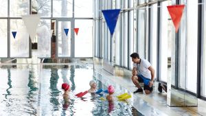 Commercial pool costs operator assisting swimmers at an indoor aquatic facility